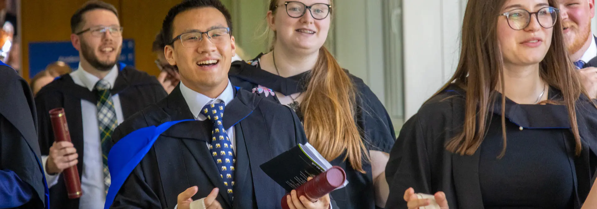Graduates smiling and walking down the corridor of Edinburgh campus.