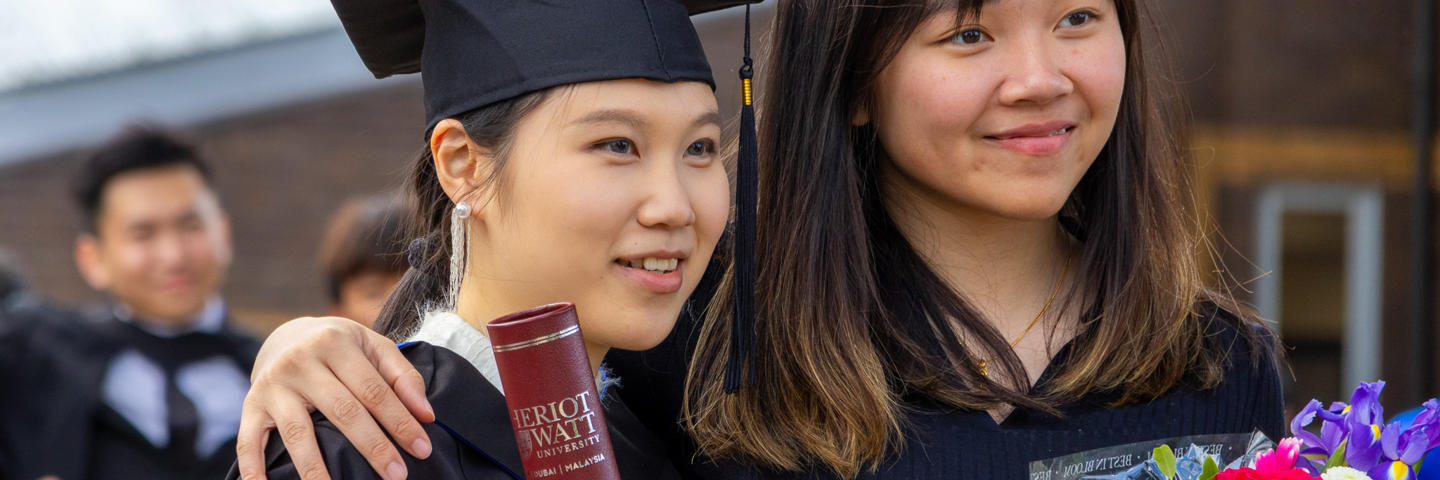 Two graduates at our Edinburgh campus posing with flowers and a certificate holder.