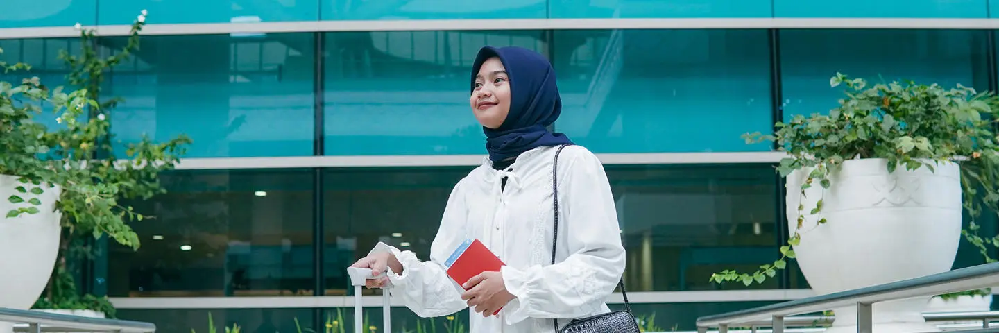A woman wearing a headscarf carrying luggage.