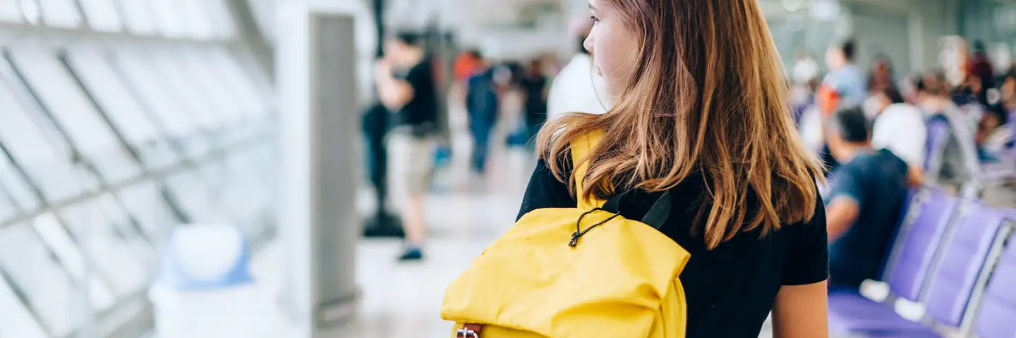 A student walking through the airport with yellow backpack.