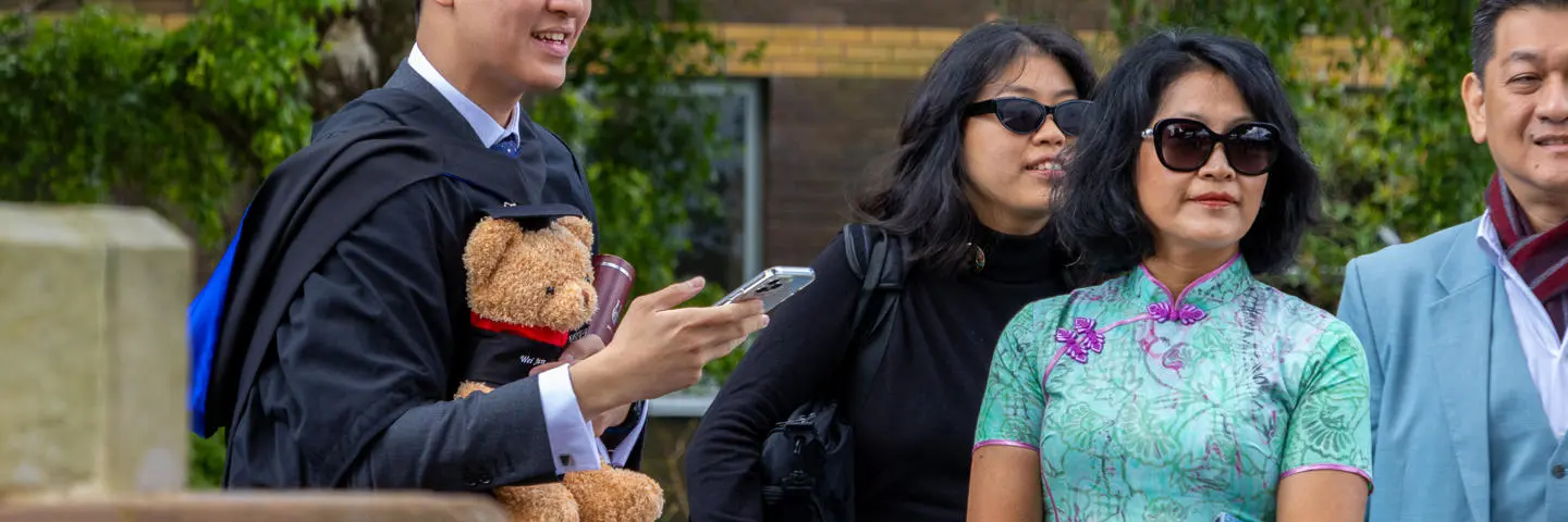 A student holding Heriot-Watt bear with family on graduation day.