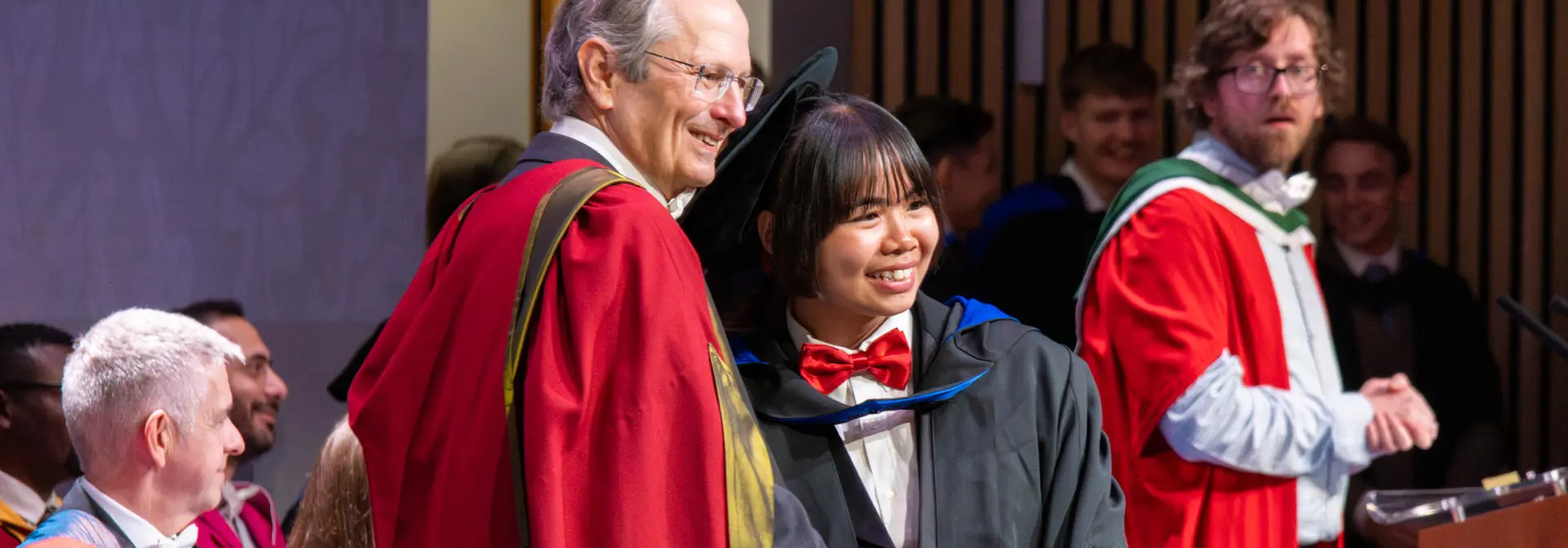 A student posing for a photo while shaking hands and receiving graduation certificate.