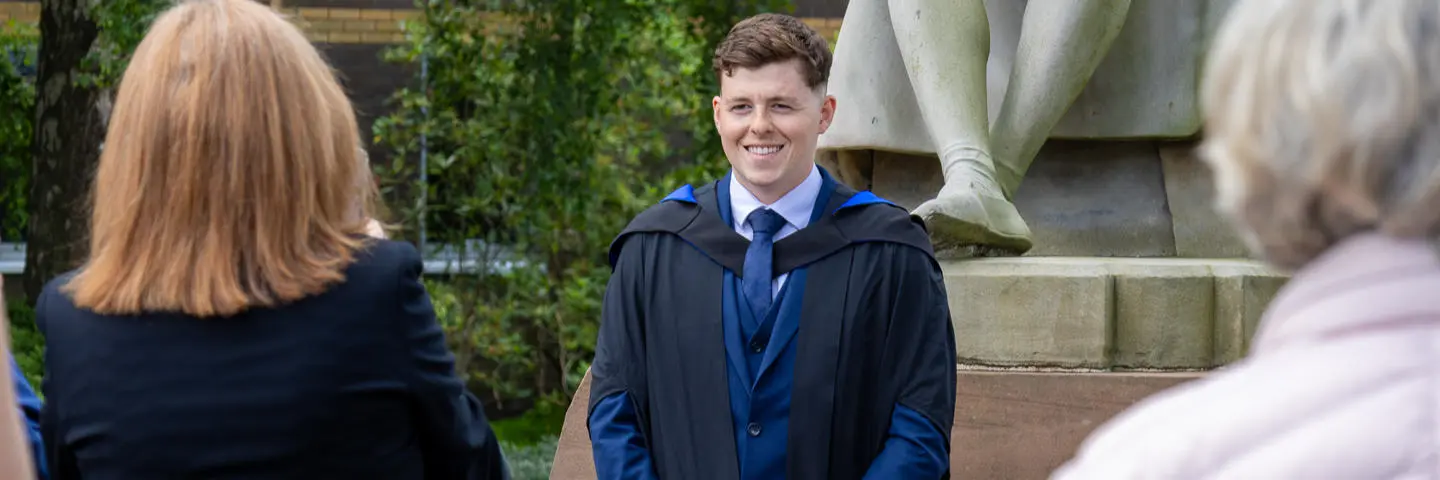 A graduate poses in front of the James Watt statue at graduation at the Edinburgh campus.