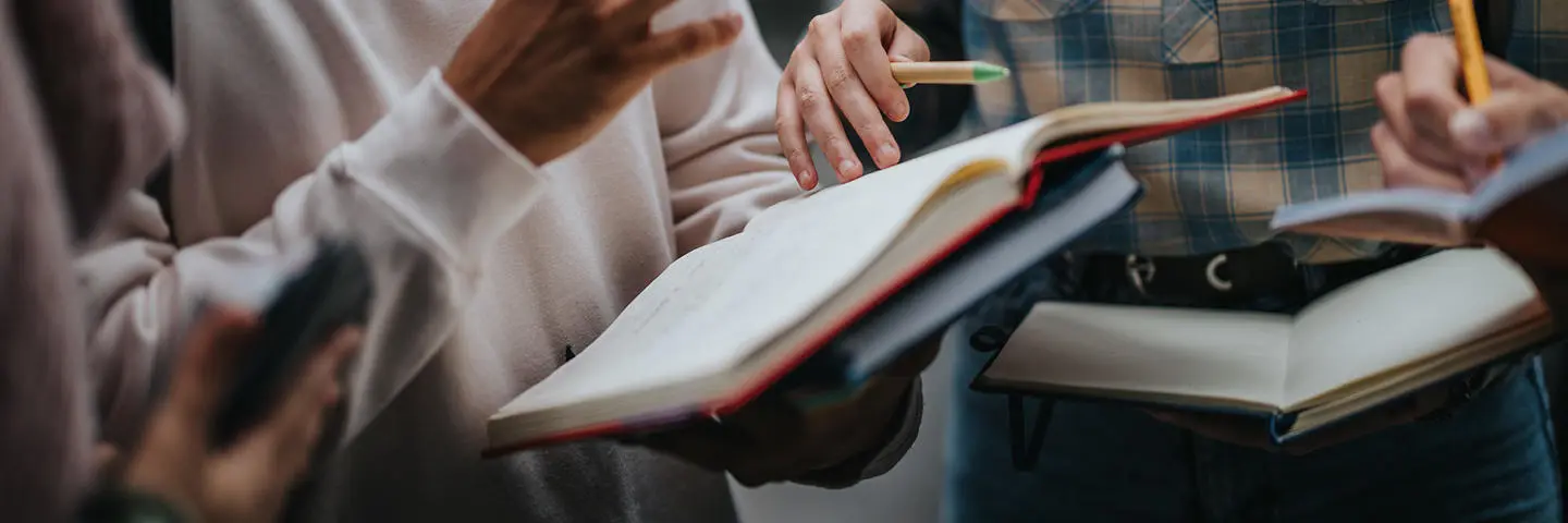 Three students in a group discussion holding books.