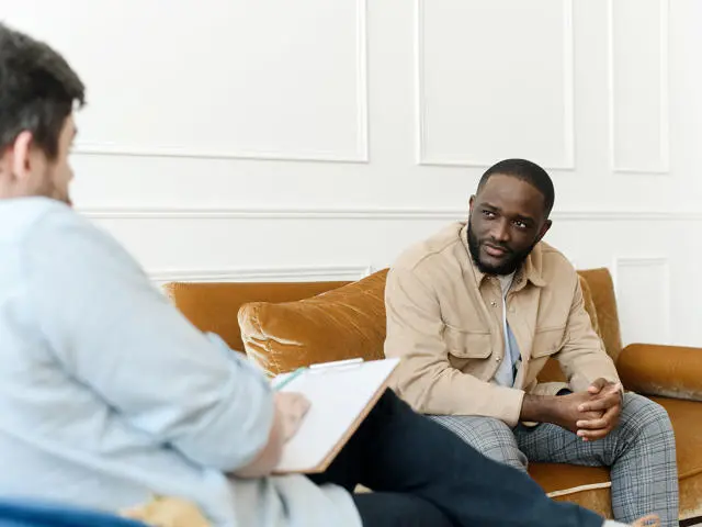 An individual sits on an orange sofa in a counselling session.