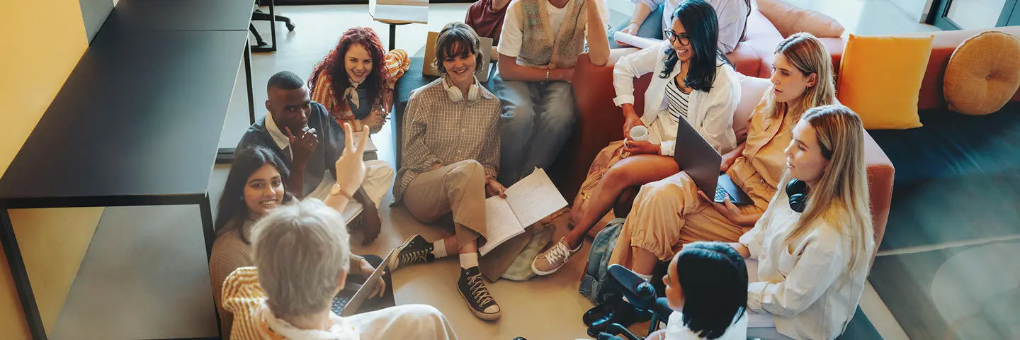 Group of students sitting in a circle on the floor and on chairs in discussion.