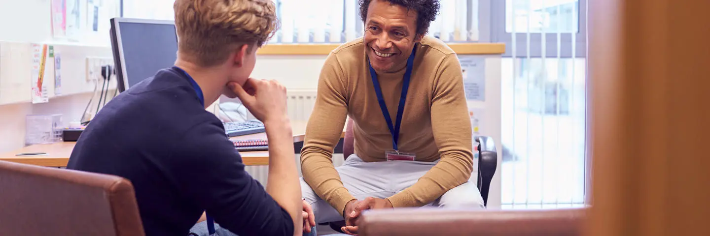 A counsellor sitting in an office talking to a student.