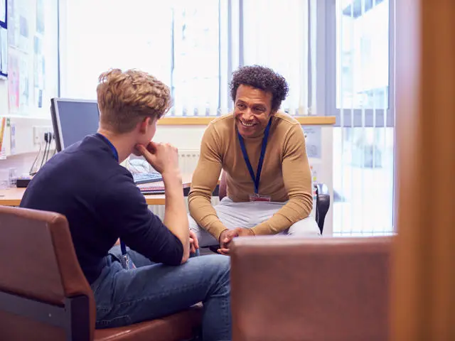 A counsellor sitting in an office talking to a student.