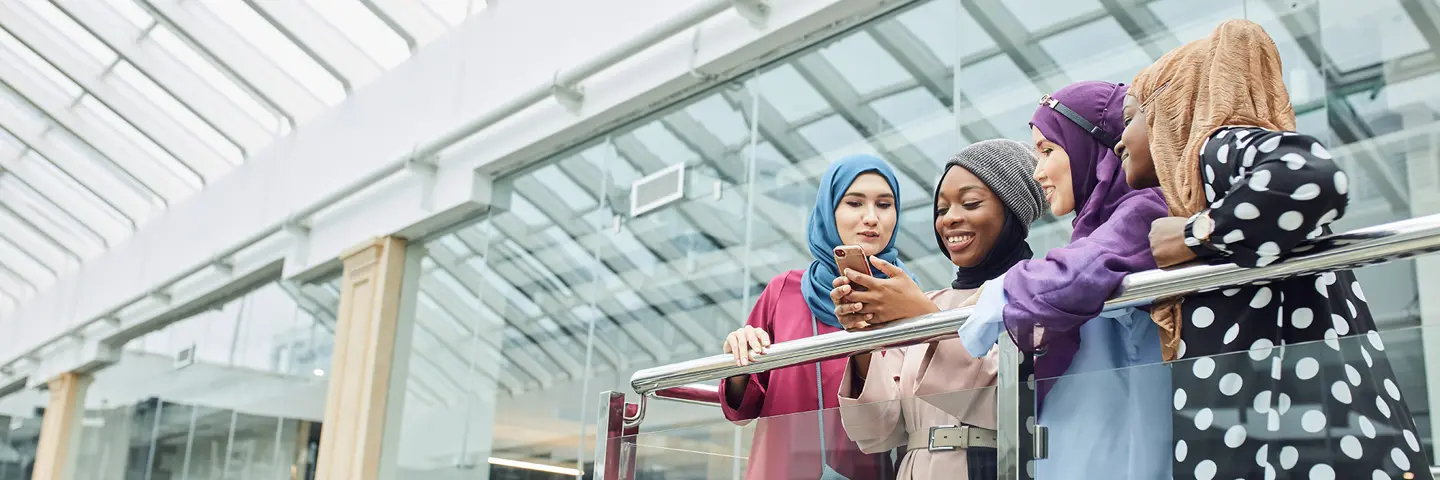 Four individuals stand looking at a phone on a balcony.