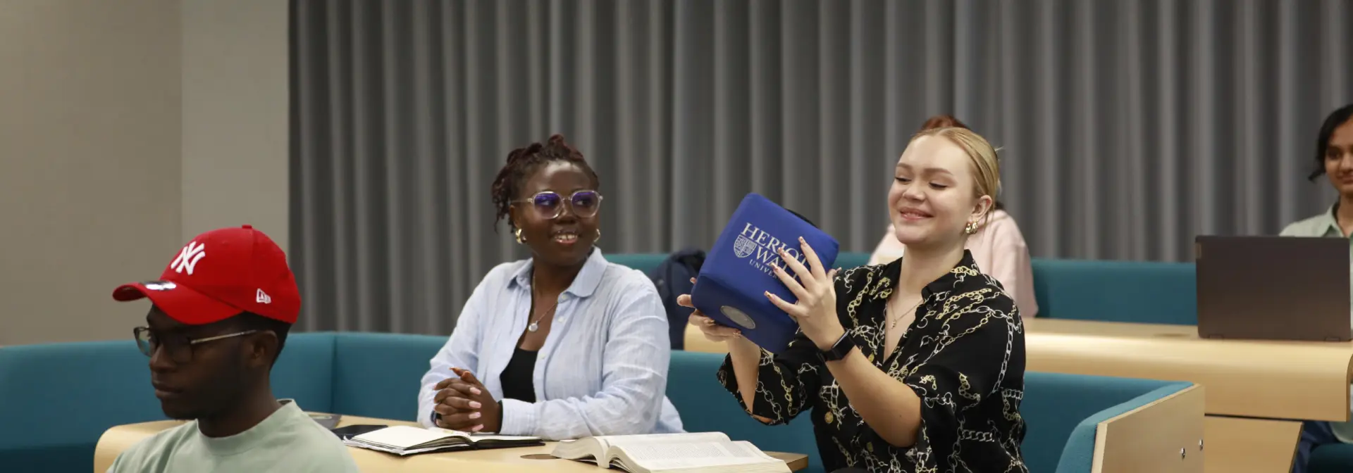 Three individuals sitting in a lecture theatre, smile as they pass around a cube.