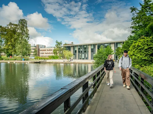 Tw individuals walking across a bridge above a loch on a sunny day.
