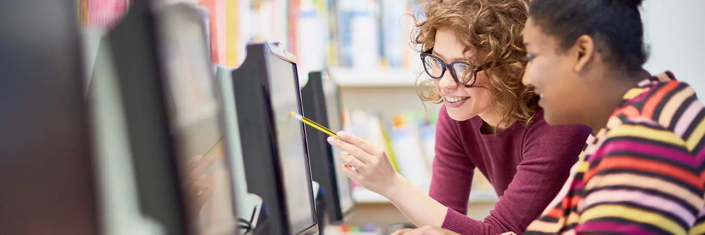 Two individuals working at a computer in a library.