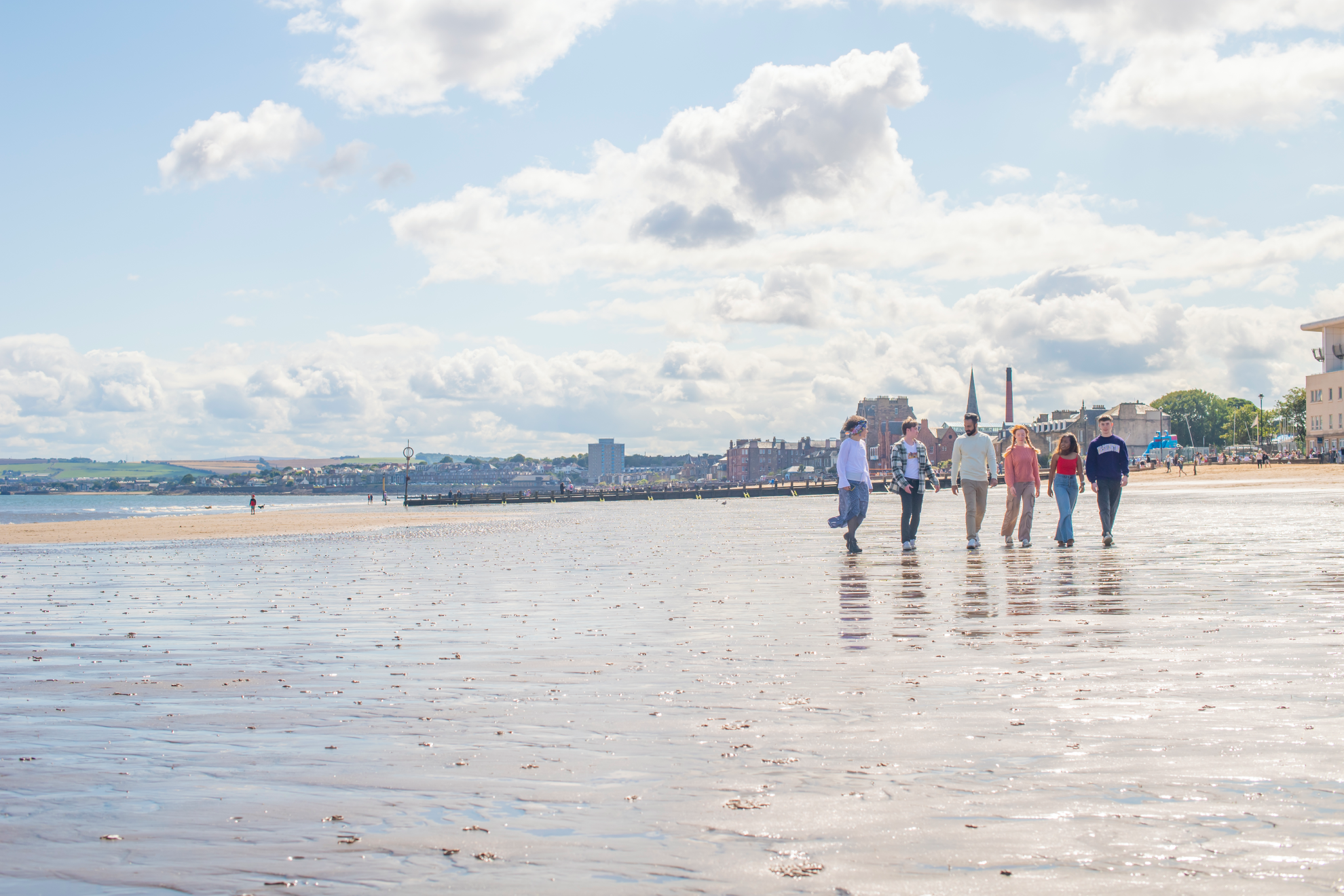 Five students walking on wet sand at Portobello beach with the town in the background.