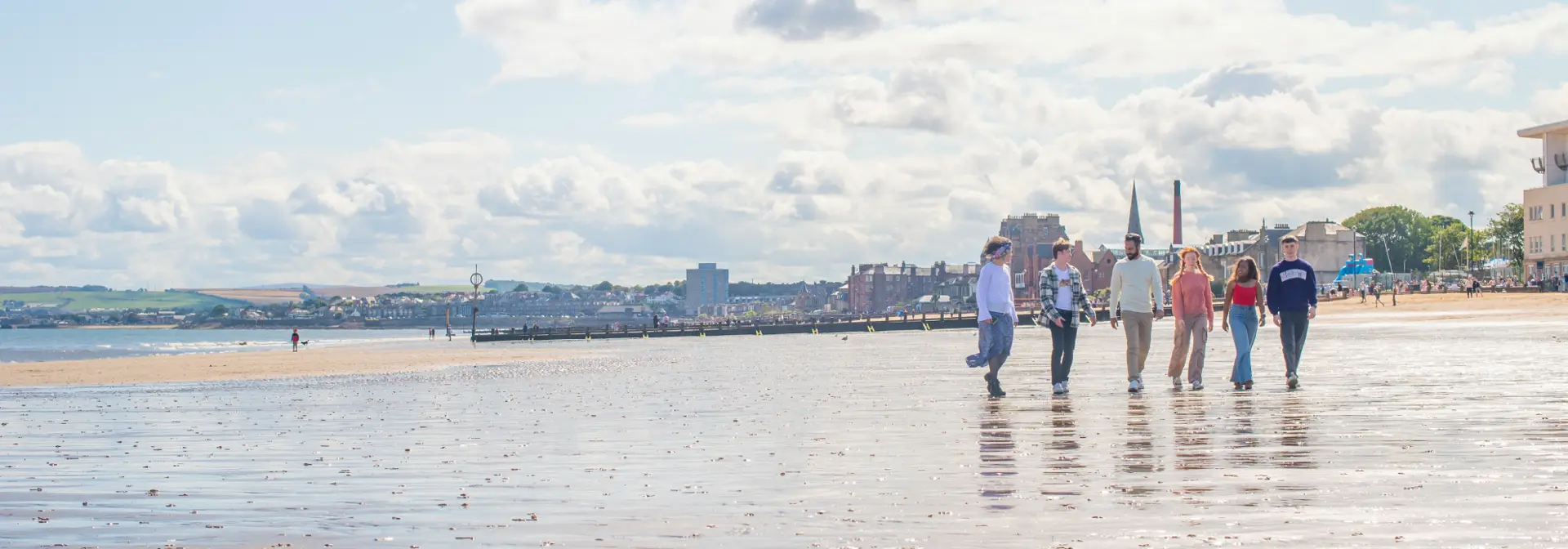 Five individuals walking on wet sand of a beach with the town in the background.