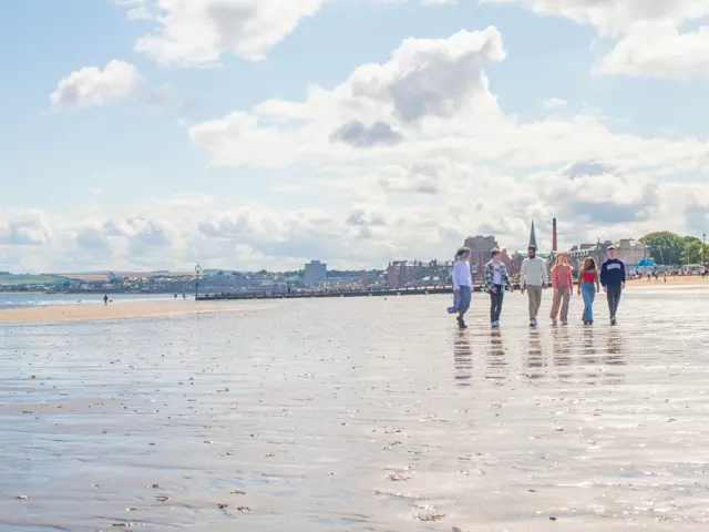Five students walking on wet sand at Portobello beach with the town in the background.
