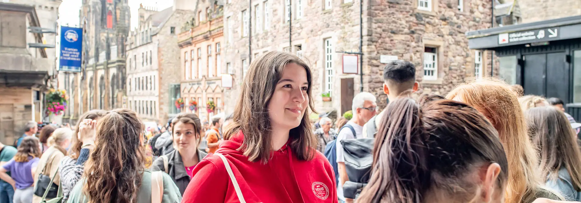 Student wearing a red hoodie and holding a canvas bag smiles in conversation.