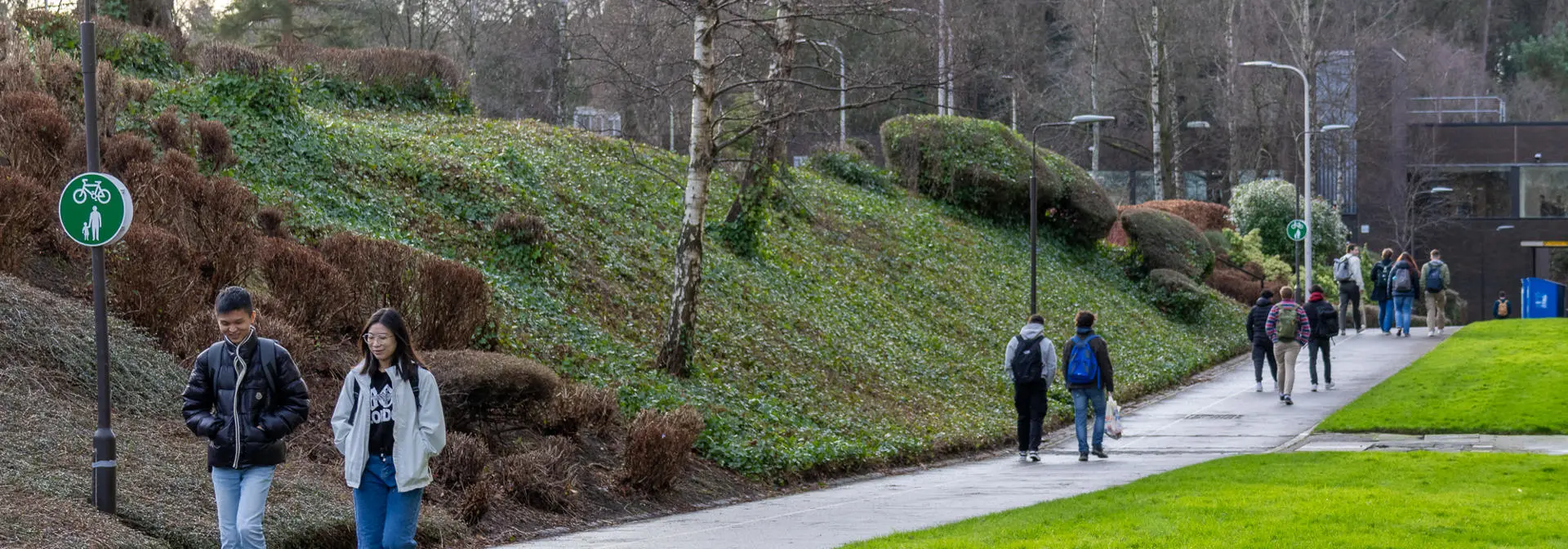 Two individuals walking along a path outside with grass and nature either side.