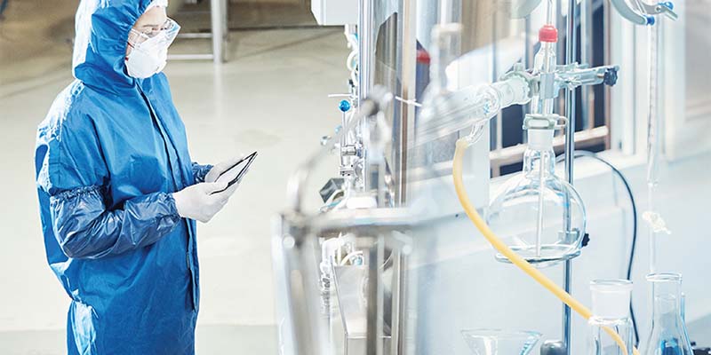 Engineer in full protective clothing and face mask inspects a chemical process