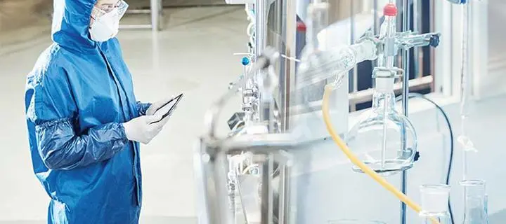 Engineer in full protective clothing and face mask inspects a chemical process