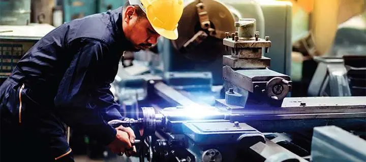 Worker wearing overalls operates a lathe in an industrial setting