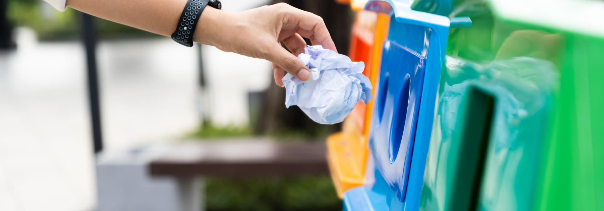 An individual puts a scrap of paper into recycling bin