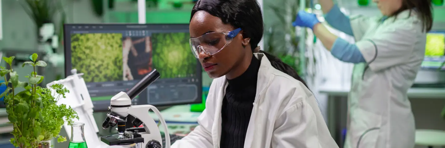 Two individuals wearing lab coats working in a laboratory with plants.