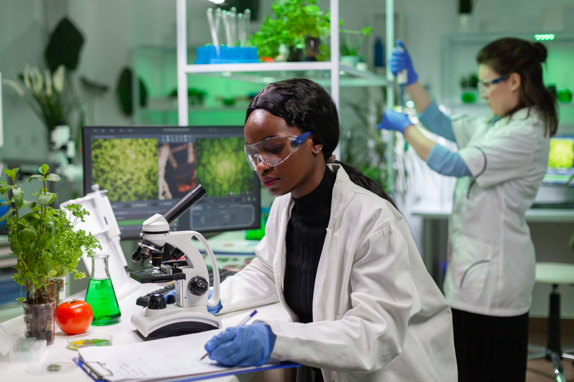 Two individuals wearing lab coats working in a laboratory with plants.