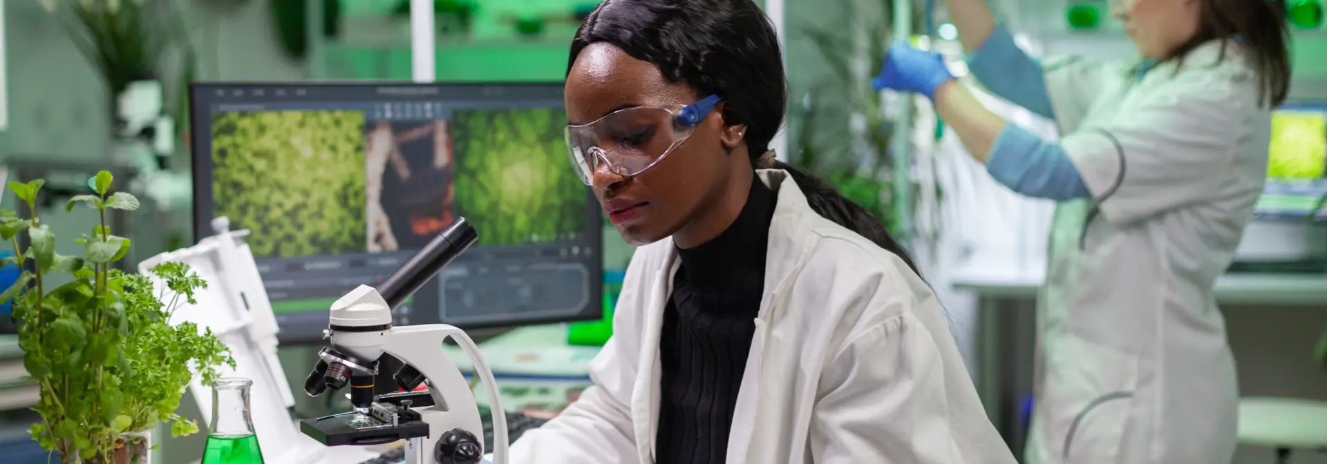Two individuals wearing lab coats working in a laboratory with plants.