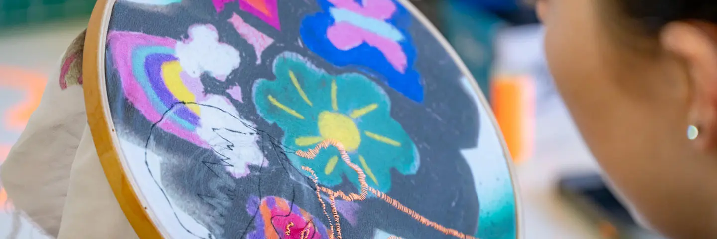 A side profile of a person as they sew and embroider a flower pattern.
