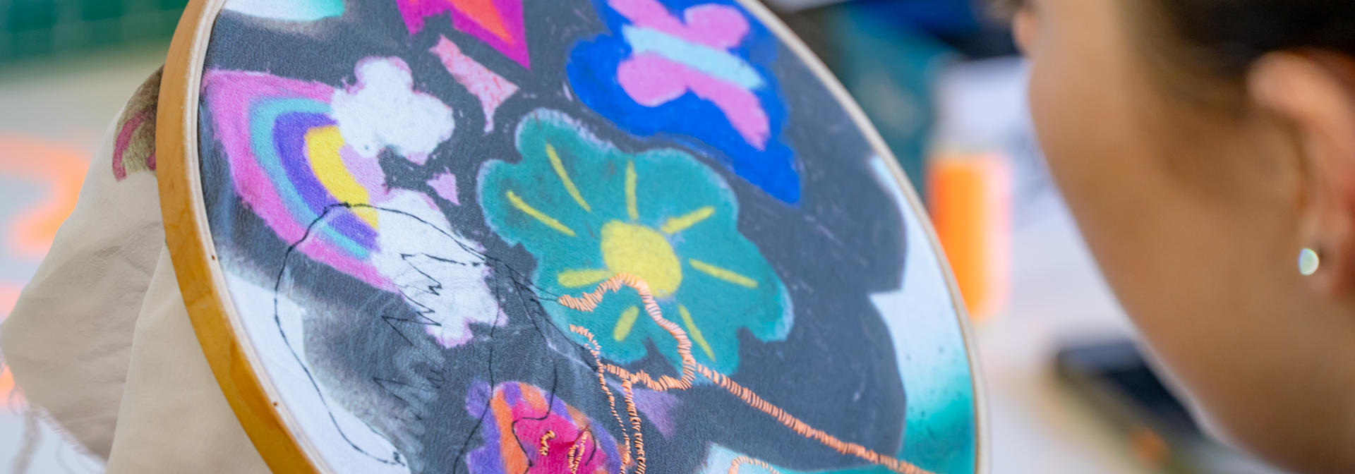 A side profile of a person as they sew and embroider a flower pattern.