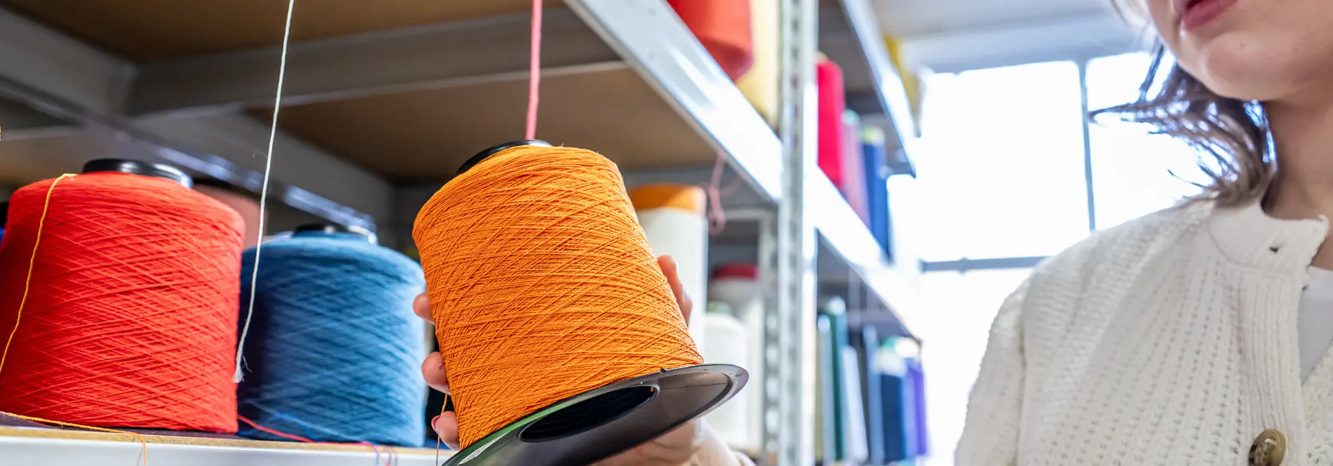 Student picking up a wheel of thread from a shelf.