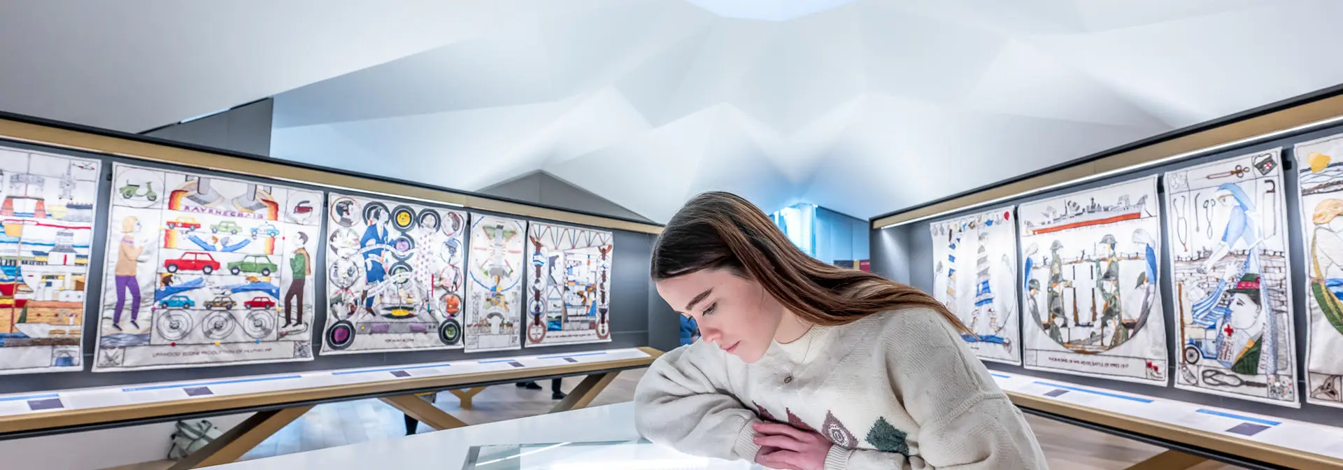 An individual in a museum, leans over a glass cabinet staring at its contents.