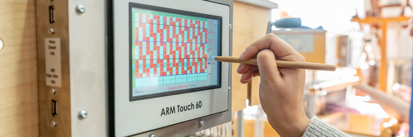 A computer screen on a weaving machine being used with a stylus.