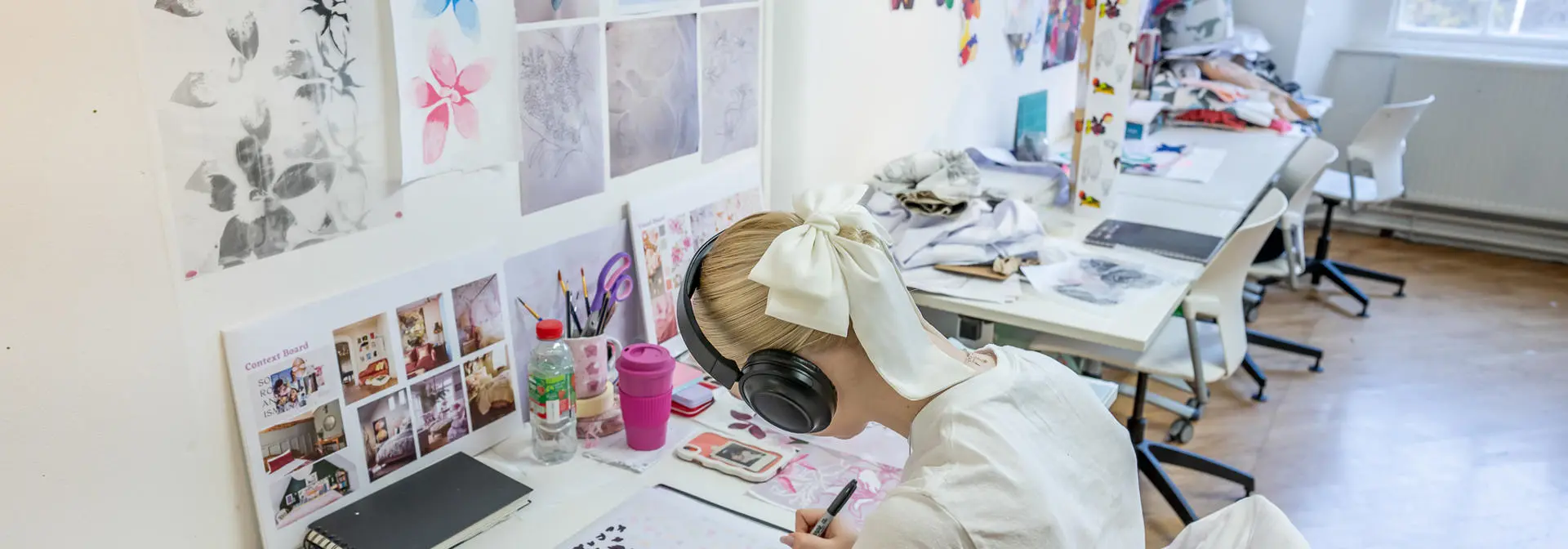 An individual leant over a desk drawing with a black pen.
