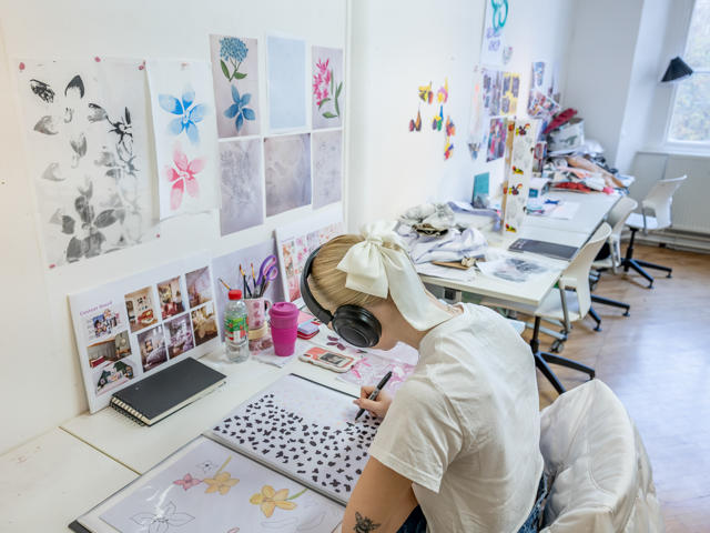 An individual leant over a desk drawing with a black pen.