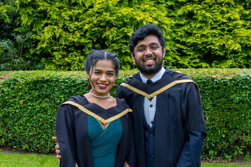 Two individuals standing in graduation robes. 