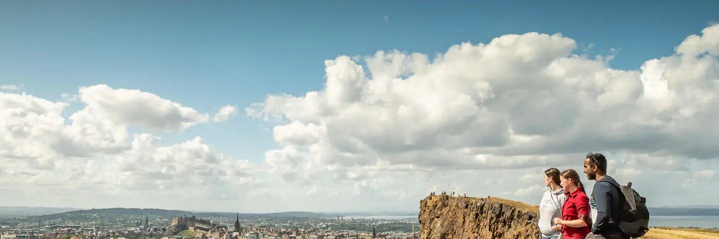 Three individuals stand atop a hill and look over at a city below.