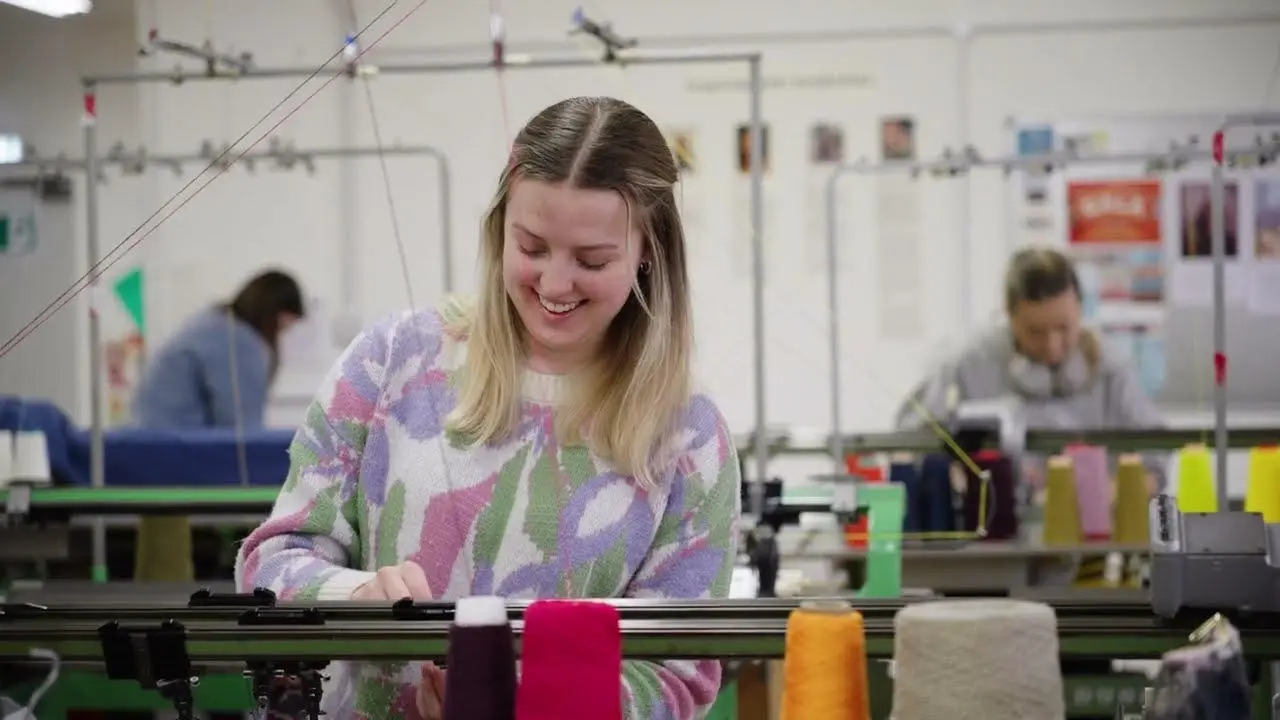 A smiling student operates a sewing machine, focused on her work.