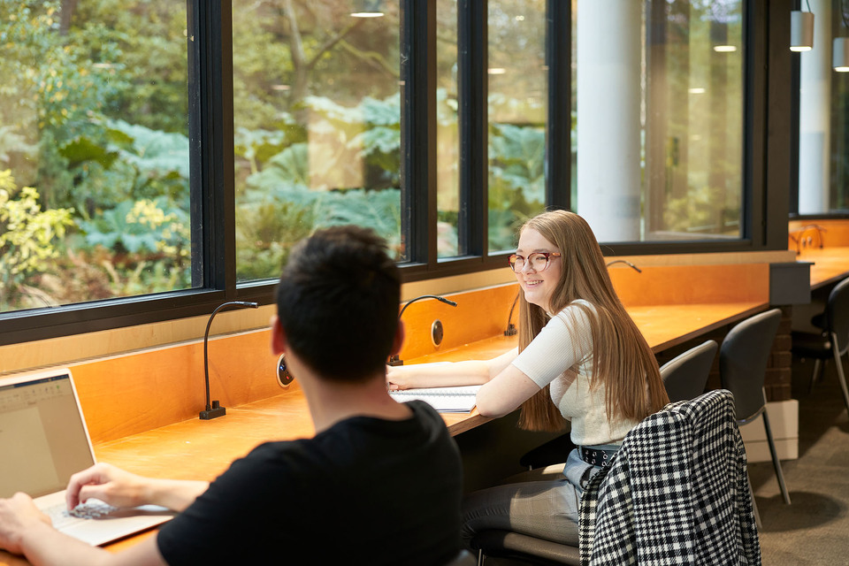 Two students sat in a study area at Heriot-Watt's Ednibrugh campus smiling and chatting