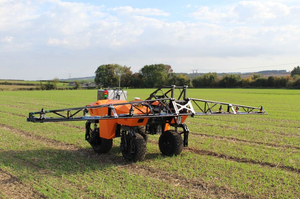 A small orange farming vehicle in a green field under a blur. It has a light metal glider on top that stretches out on either side.