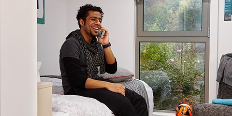 Male student chatting on phone in postgraduate accommodation