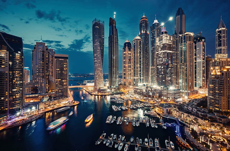 Dubai city skyline illuminated at night with boats moored in the harbour