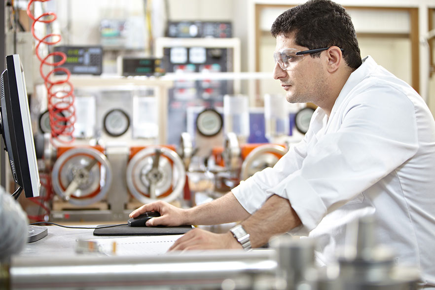 Male in lab coat and safety goggles working at computer