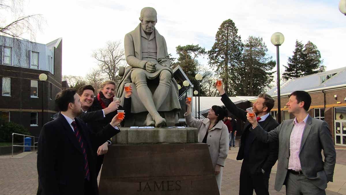 Alumni group raise their glasses to the statue of James Watt outside the main reception, Edinburgh Campus