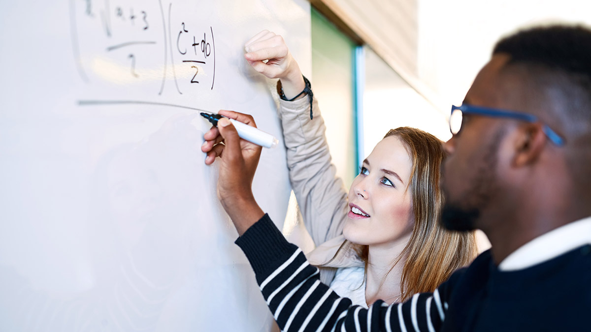 Two students or colleagues work on an equation on a whiteboard