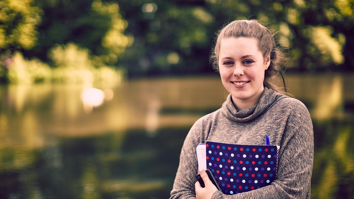 Female student holding a folder beside the loch in summer, Edinburgh Campus