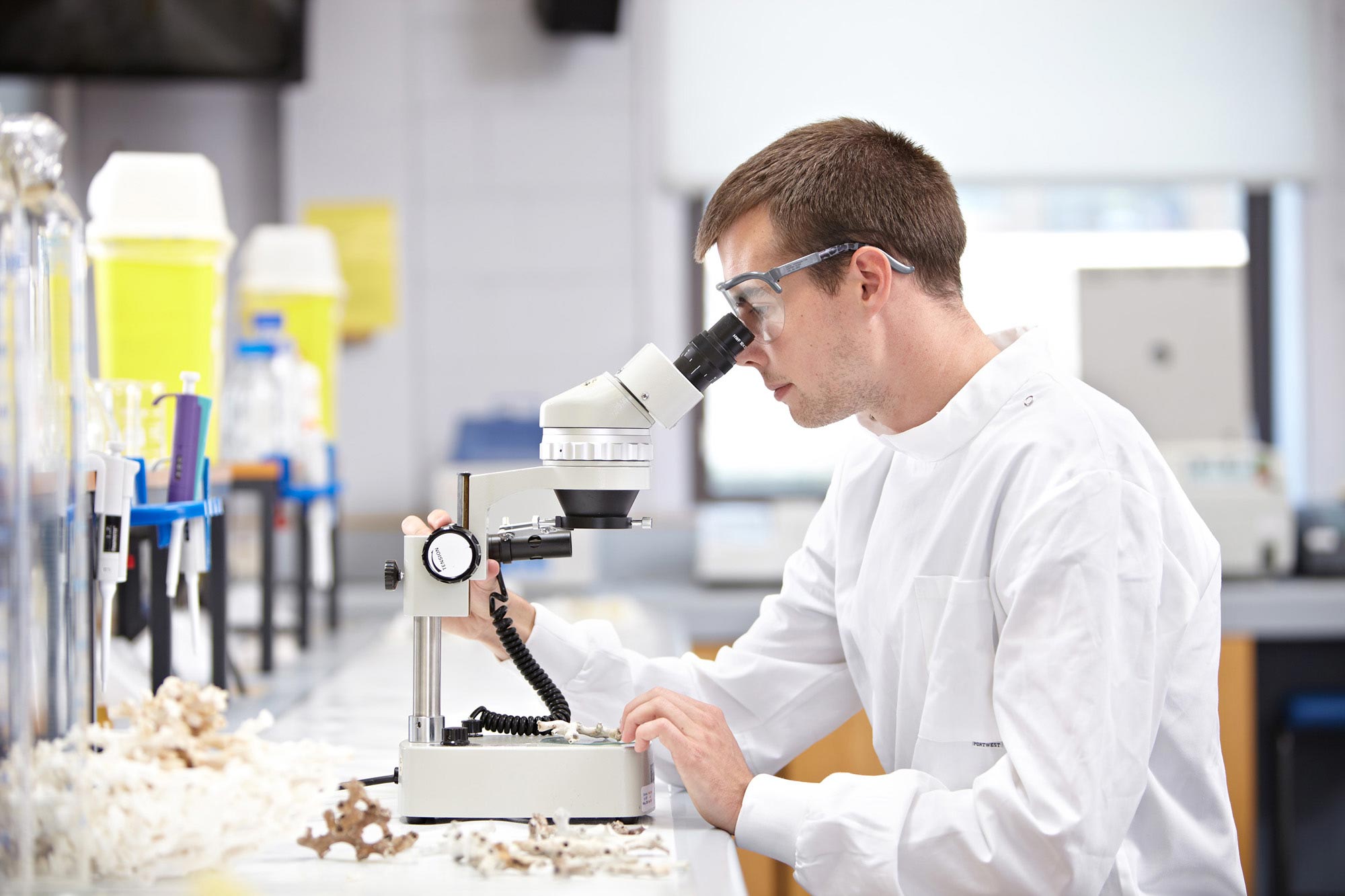 Student wearing goggles and using microscope