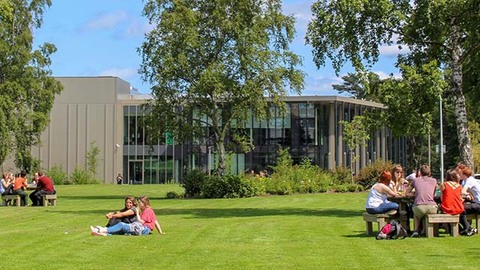 Students sitting on the grass and at picnic tables in front of the GRID building, Edinburgh Campus