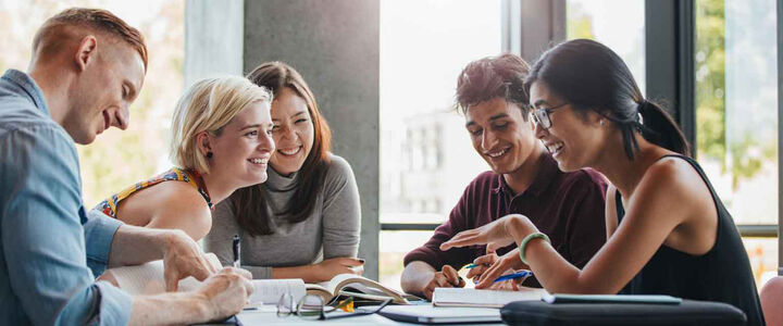 A group of students around a table share a laugh while working