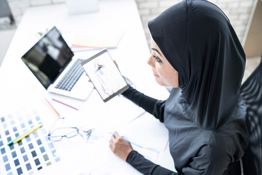 Woman holding tablet over desk of design drawings